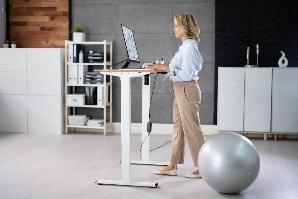 A woman working at an adjustable standing desk setup in an office setting, maintaining an ergonomic posture.